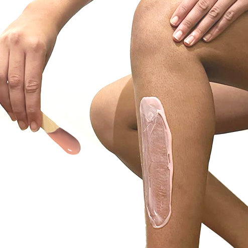 Application de cire rose chaude à l'aide d'une spatule sur la jambe